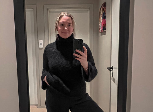 Kvinne som tar selfie i et speil, har på seg en elegant og svart strikkegenser og svarte løstsittende bukser